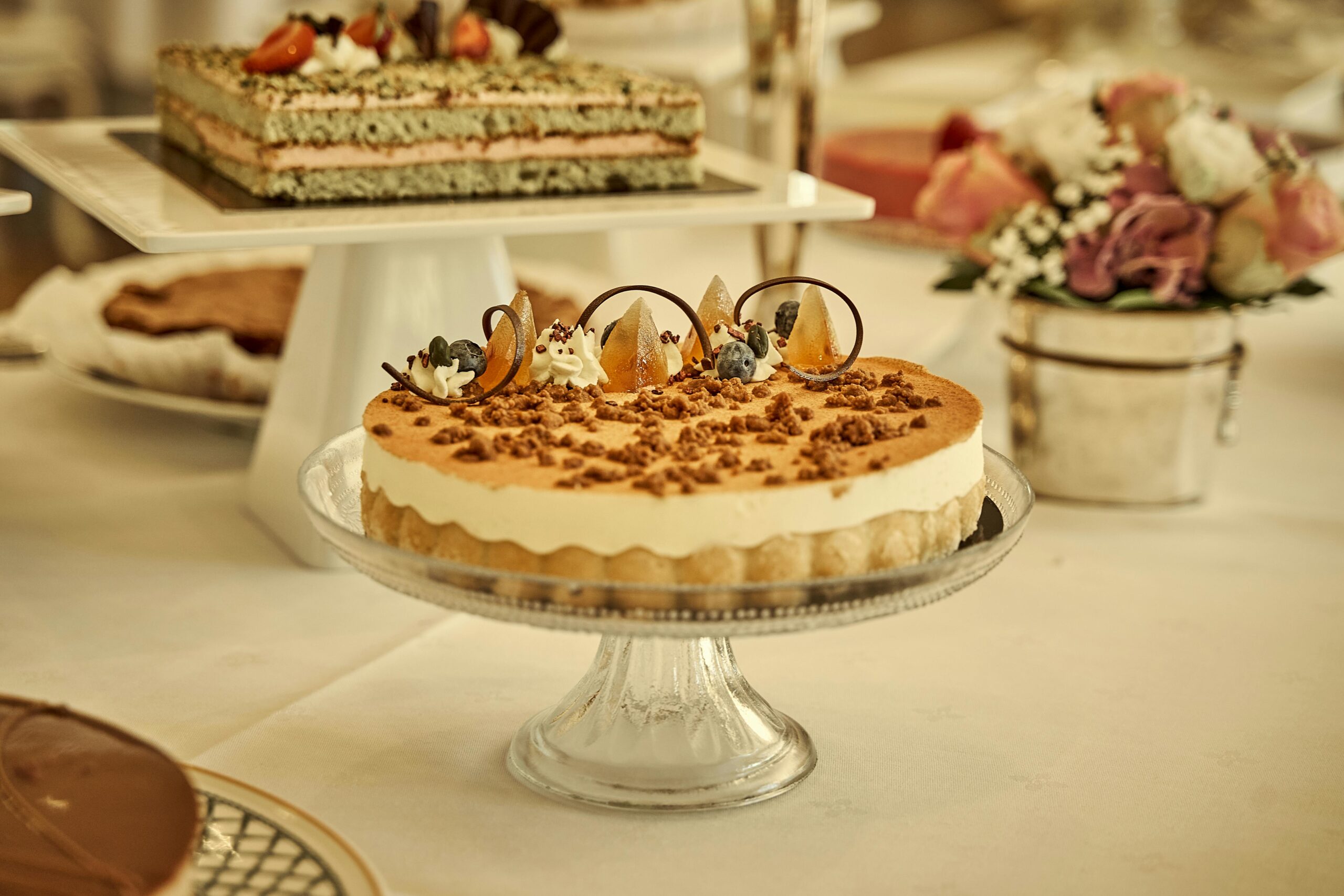 A beautiful assortment of gourmet desserts including a highlighted mousse cake on a glass stand.