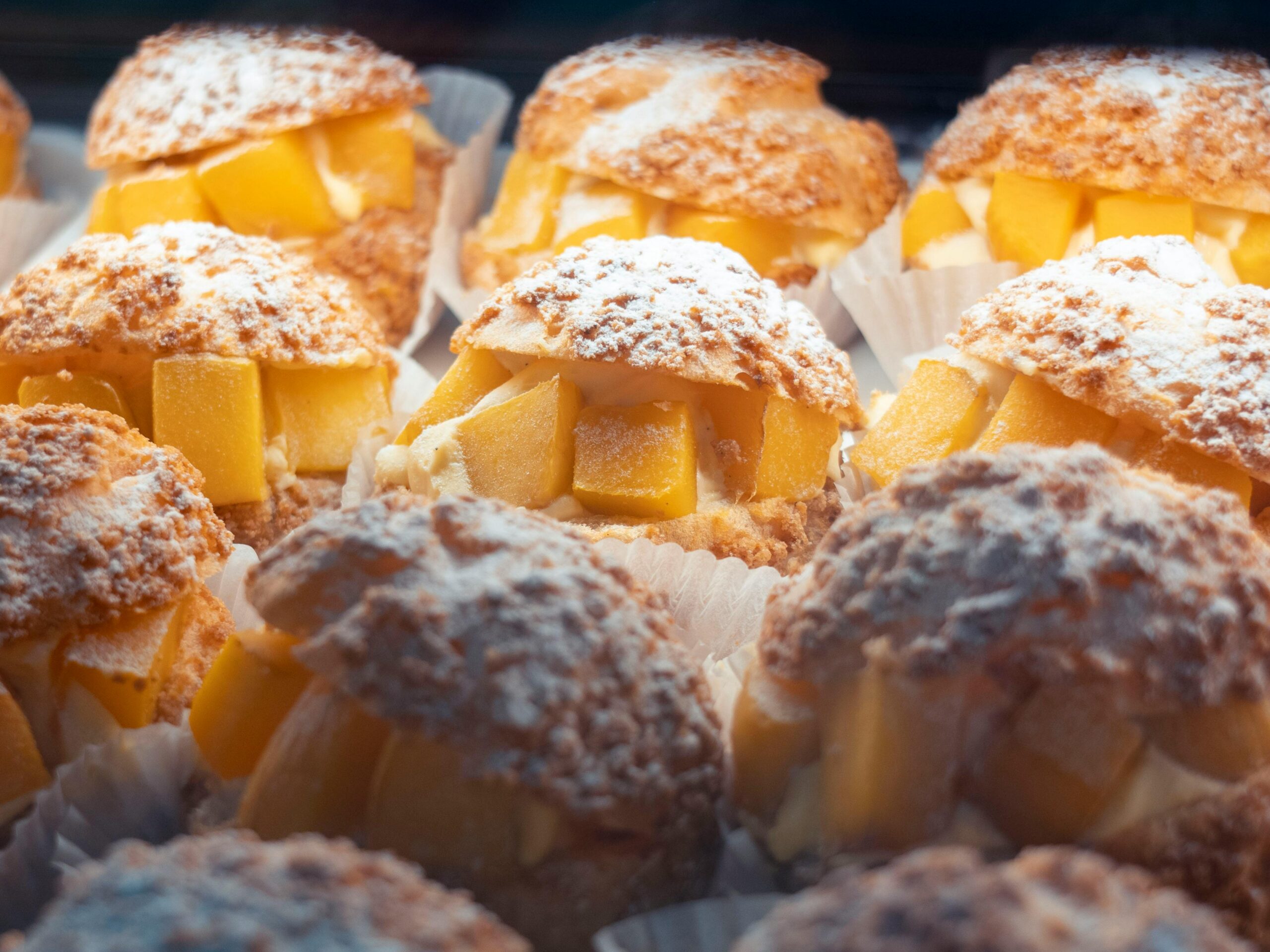 Indulgent mango cream puffs topped with powdered sugar, perfect for dessert lovers.